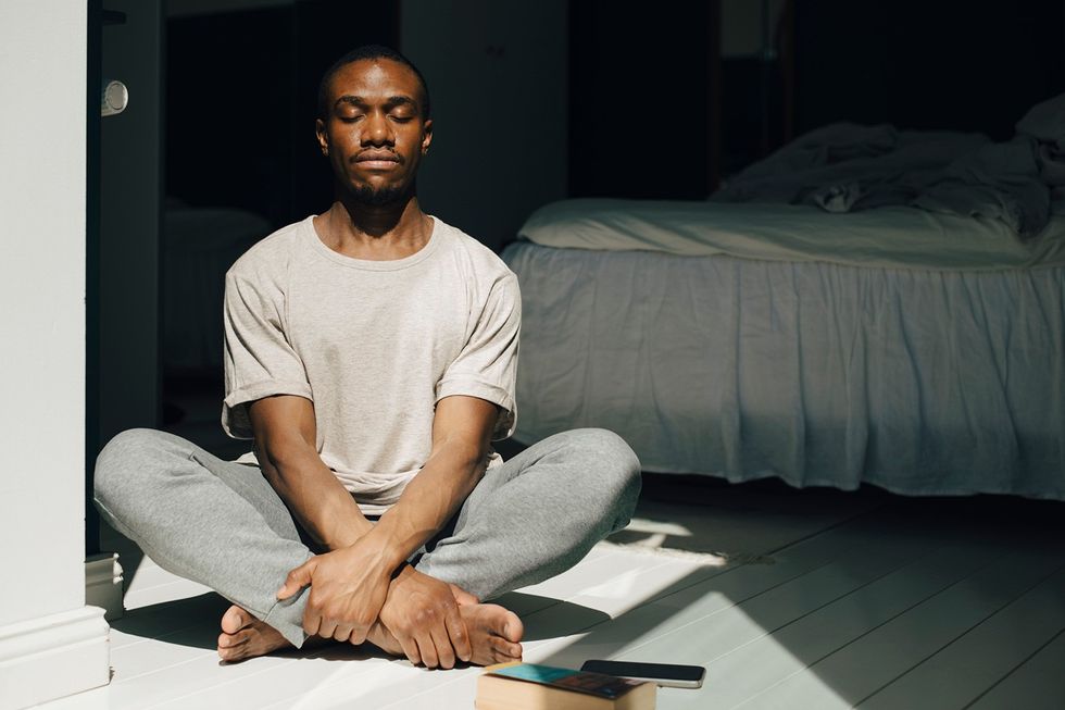 Mid adult man meditating with eyes closed in sunlight at home